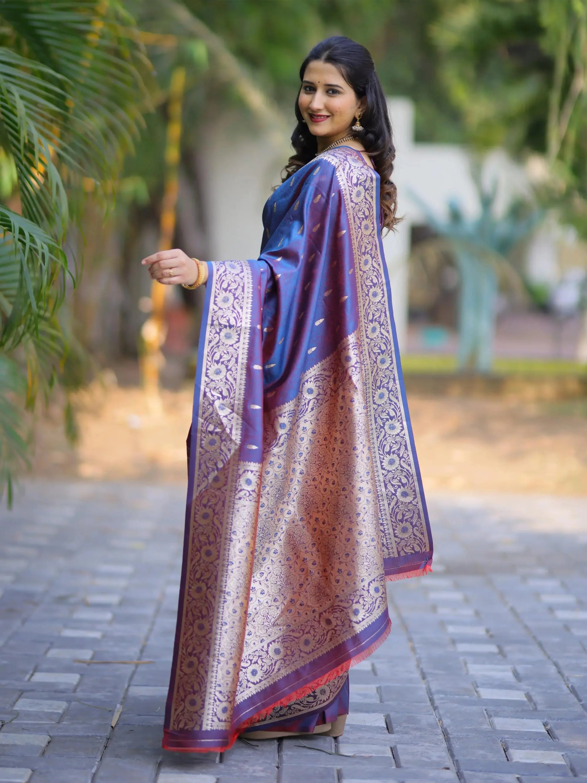Woman wearing a traditional saree with a blue and gold pattern, standing outdoors.